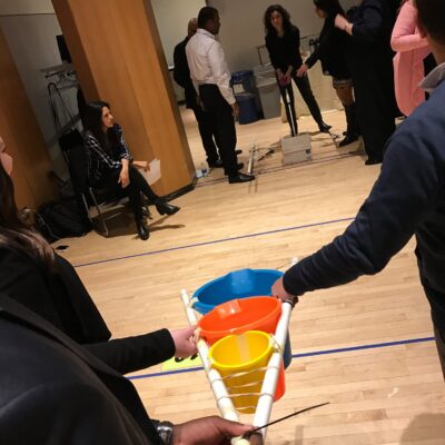 Participants in a team building activity indoors, holding a structure with colorful buckets as part of the Catapult to Success event, focusing on teamwork, coordination, and strategic planning. thumbnail