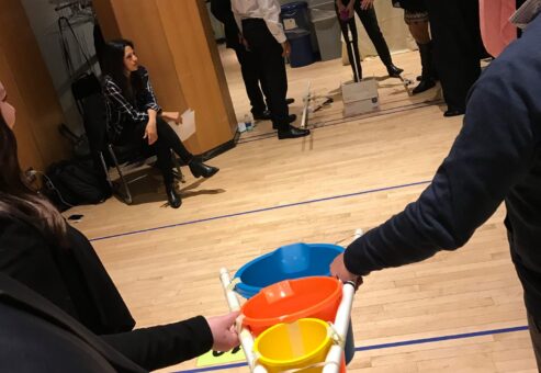 Participants in a team building activity indoors, holding a structure with colorful buckets as part of the Catapult to Success event, focusing on teamwork, coordination, and strategic planning.