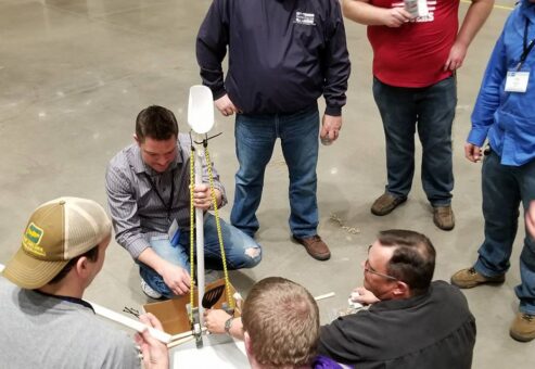 A group of participants indoors gathered around a table, actively assembling a catapult as part of the Catapult to Success team building activity, focusing on collaboration, innovation, and hands-on problem-solving.