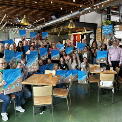 Group showcasing their ocean-inspired paintings after a creative session during a Mystery Bus team building event. thumbnail
