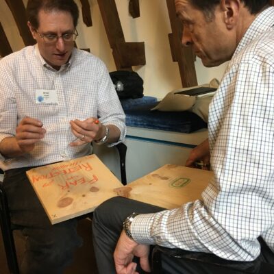 Two participants engage in a reflective moment, writing on wooden boards during a board-breaking team building event aimed at overcoming personal and professional barriers. thumbnail