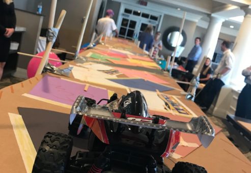 A remote-controlled car prepares to cross a large cardboard bridge designed by participants during the Bridging the Divide team building event.