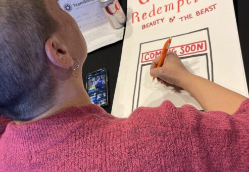 A participant draws a poster titled 'Gaston's Redemption: Beauty & The Beast' during a team building activity, showcasing creativity.