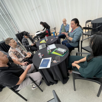 Group of team members sitting around a round table engaged in discussion on how to make a movie and what story to tell during the Corporate Film Festival team building. thumbnail