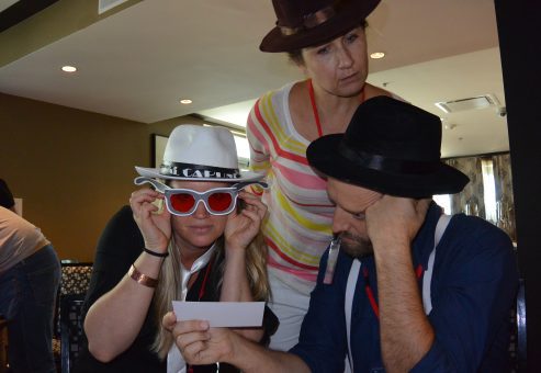 A team participating in the Escape the Mob event focuses on solving clues, while wearing fun mobster-themed hats and sunglasses to fit the robbery mystery challenge.