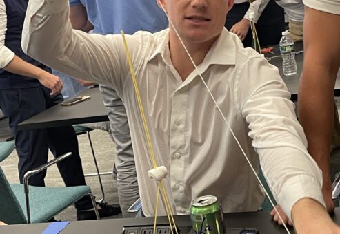 A participant at a corporate team building event working on a hands-on challenge, constructing a tower using spaghetti and marshmallows. The activity encourages problem-solving, creativity, and teamwork.