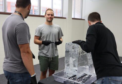 A group of participants works together, chiseling an ice block during a Team building Ice Sculpting event, showcasing teamwork and creativity.