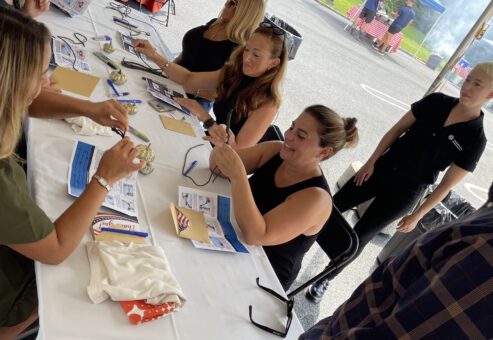 Group of people sitting at a table outdoors working on a team building activity with various materials during a corporate charitable activity.