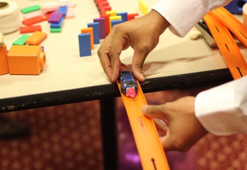 Close-up of a participant placing a toy car on a track as part of a hands-on activity during the Domino Effect team building event.