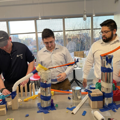 Team members collaborating to construct a creative machine in the Domino Effect team building event. thumbnail