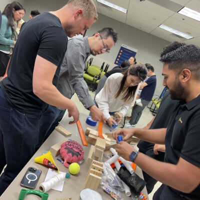 Group of participants collaboratively constructing a Rube Goldberg-style machine during the Domino Effect team building event. thumbnail