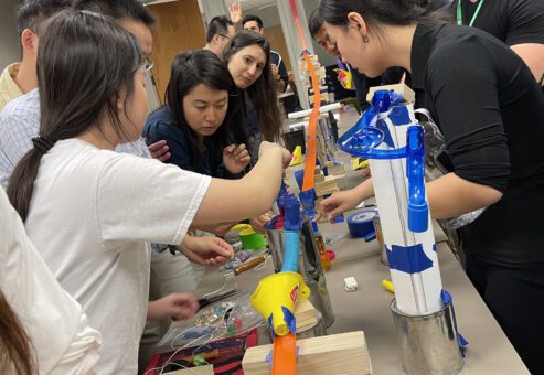 A group of participants collaborates to assemble a complex chain reaction during the Domino Effect team building activity, focusing on constructing innovative contraptions.