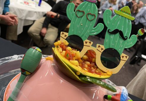 A festive salsa presentation featuring a bowl of fresh salsa garnished with playful cactus-shaped glasses, maracas, and a mini piñata, capturing the lively spirit of the Salsa Showdown team building event.
