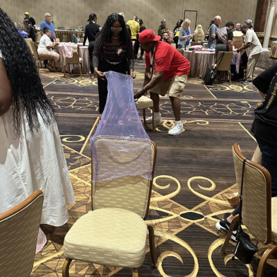 Two participants in a team building activity are working together to cover a chair with a transparent purple material. The man is securing the fabric at the bottom, while the woman stretches the material across the back of the chair. thumbnail