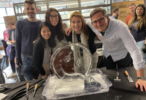 A team poses proudly beside their nearly completed ice sculpture during a Team building Ice Sculpting event, demonstrating collaboration and creativity.