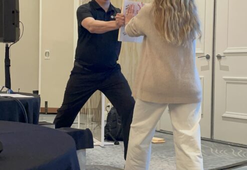 A facilitator guides a participant through a board-breaking exercise during a transformative team building event focused on overcoming barriers.