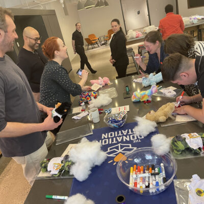 Group of participants smiling and working together at a table filled with supplies during a corporate charitable team building event called The Donation Station. thumbnail