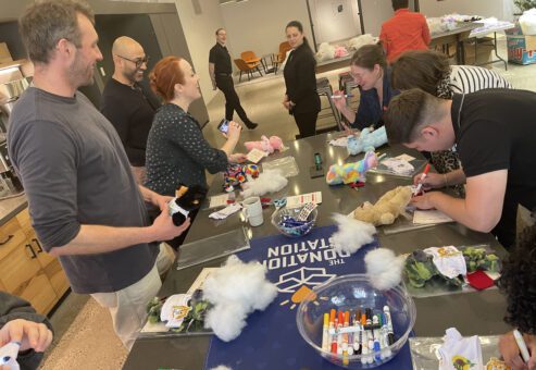 Group of participants smiling and working together at a table filled with supplies during a corporate charitable team building event called The Donation Station.