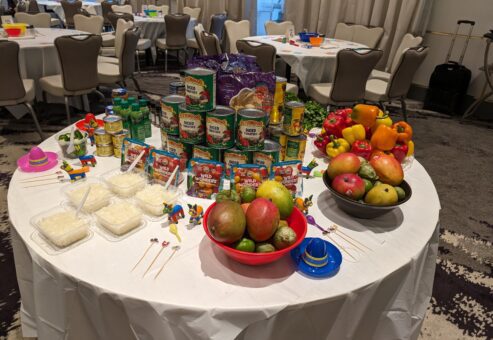 A vibrant setup of fresh fruits, including mangoes and peppers, along with canned ingredients for the Salsa Showdown team building event, featuring colorful decorations.