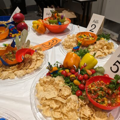Colorful bowls of salsa and fresh ingredients, surrounded by tortilla chips and labeled for different teams during the Salsa Showdown team building event. thumbnail