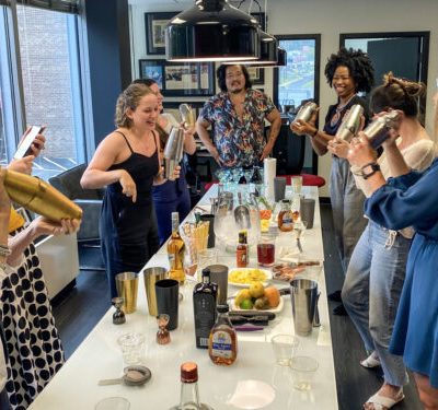 Team shaking cocktail shakers in a mixology class, enjoying the process of creating drinks together. The event promotes collaboration, creativity, and teamwork in a fun and interactive setting. thumbnail