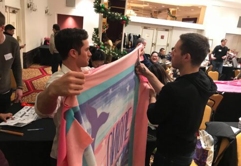Two team members work together to prepare a fleece blanket during a holiday-themed team building event, contributing to gifts for seniors as part of the Hope for the Holidays program.