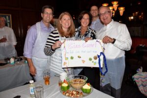 Team of participants proudly presenting their dish and a decorated sign during the Wicked Good Chowda Cook-Off team building event.