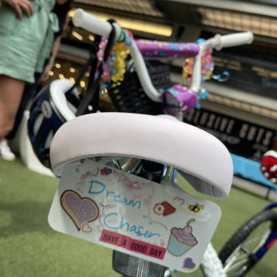 Close-up of a decorated bicycle from a Charity Bike Build event. The bike seat features a personalized tag reading 'Dream Chaser' with colorful stickers, including hearts, a cupcake, and motivational text 'Have a Good Day,' showing thoughtful details in the bike assembly process. thumbnail