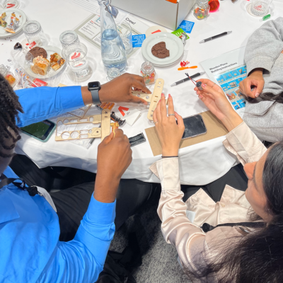Participants working together at a table, assembling parts of a miniature airplane from a STEM kit during the STEM Speedway team building activity, focusing on teamwork, precision, and hands-on learning. thumbnail